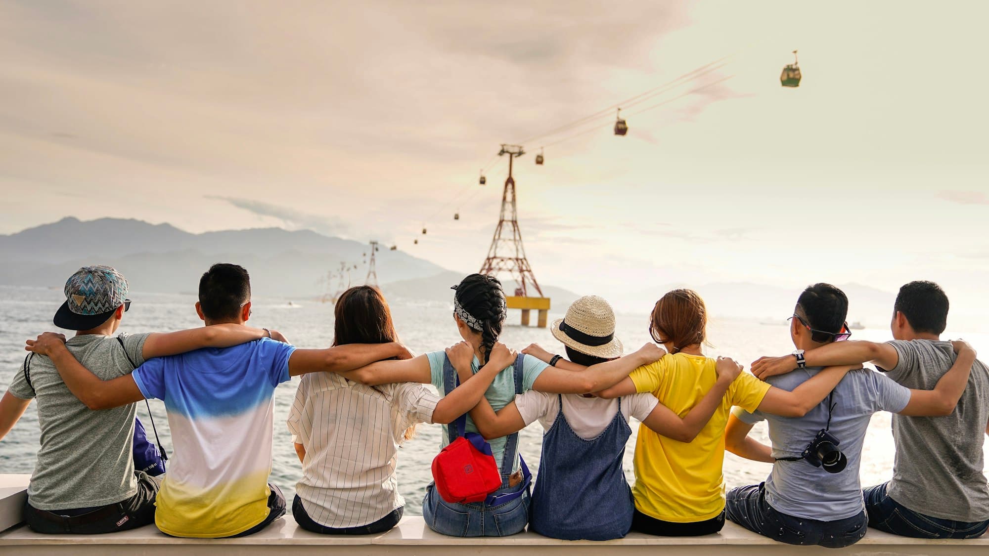 Teenagers with arms around each other looking out over water at sunset