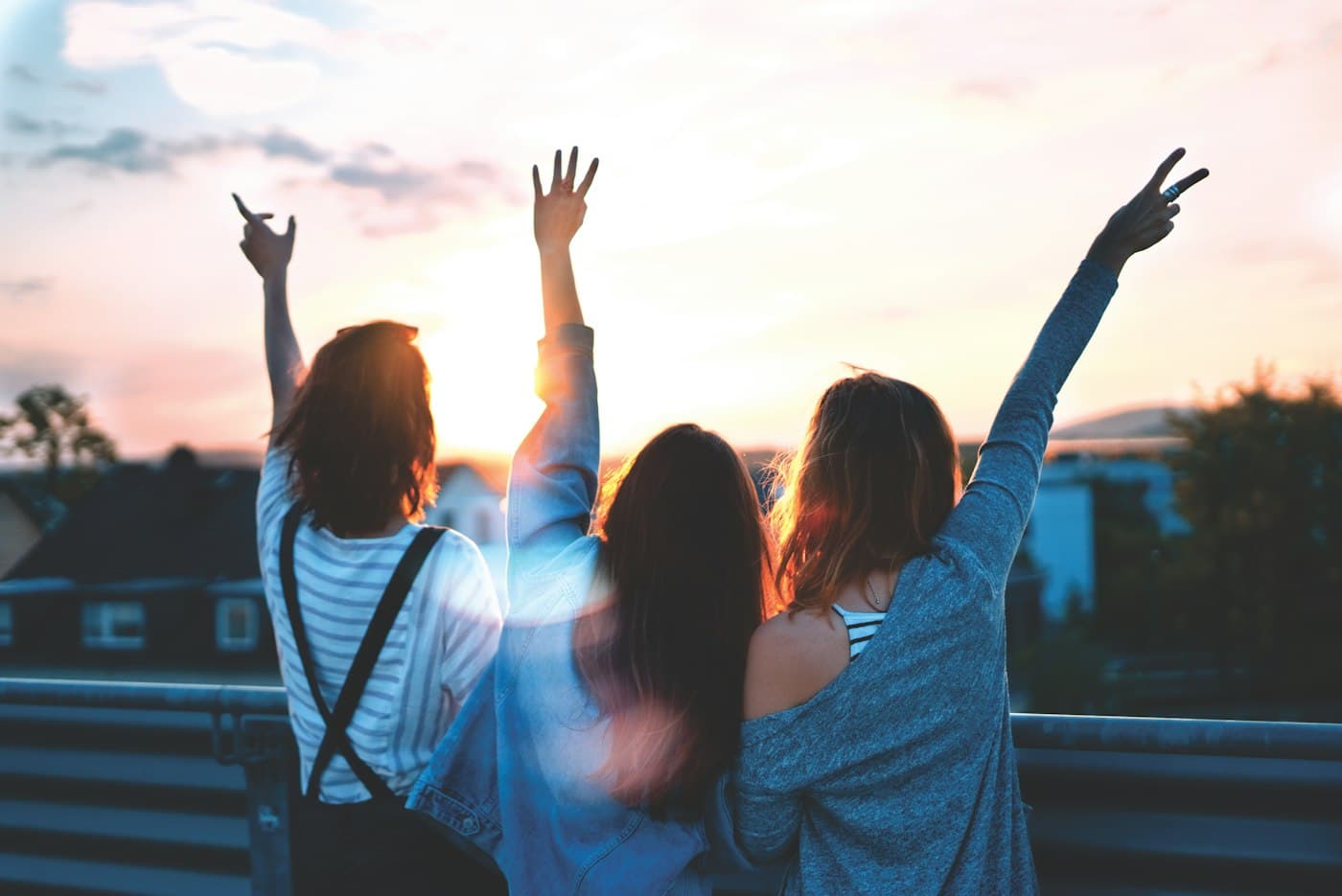 Young people viewed from behind raising their hands at sunset